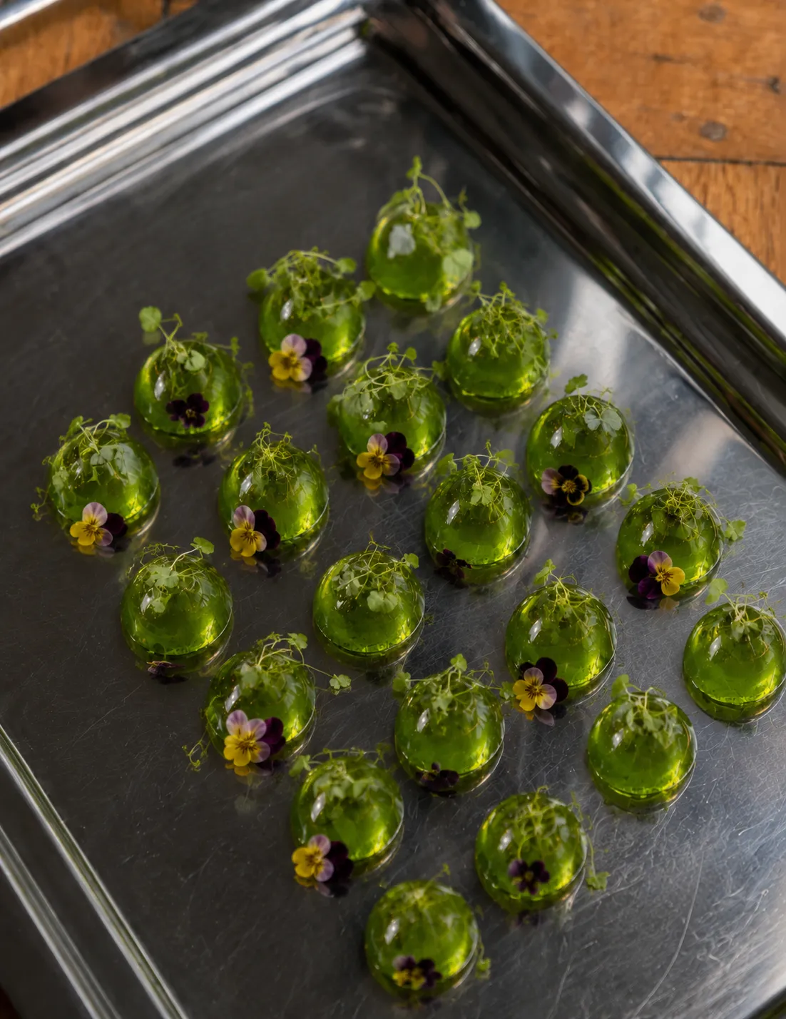 Green herbal domes finished with edible flowers on a tray